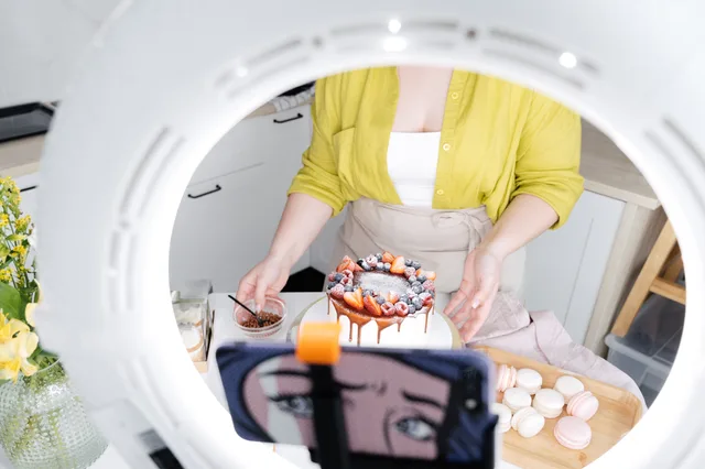 Crop faceless female confectioner taking photo on cellphone of delicious decorated cake and macaroons using ring light lamp. How ASA and CMA rules decide what UK food creators must label