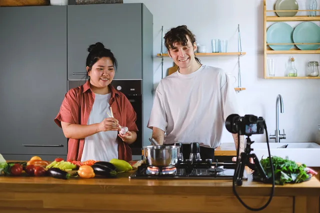 Two vloggers cooking and filming culinary content in a stylish kitchen setup. Plan your food creator partnerships tools and providers