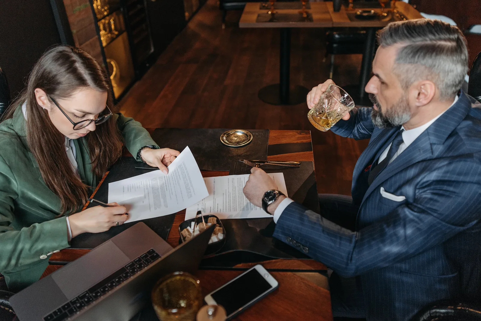 A man and woman in a business meeting, signing documents over drinks in a stylish restaurant.